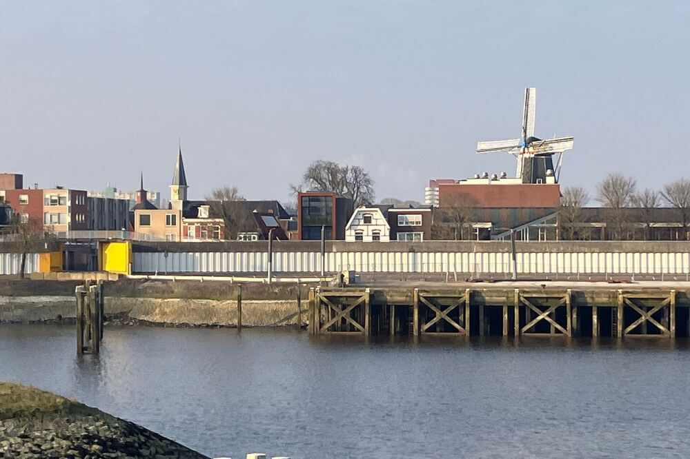 Stadsgezicht van Delfzijl vanaf het water met een molen en kerktoren boven de kade