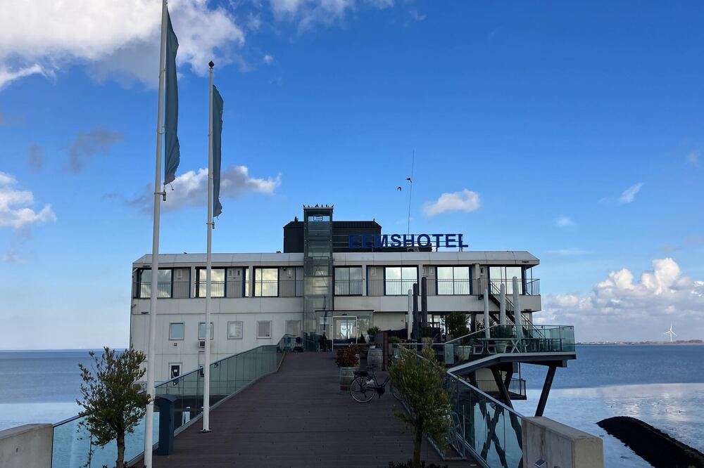 Het Eemshotel op palen in het water van de Eems bij Delfzijl, met een houten steiger ernaartoe